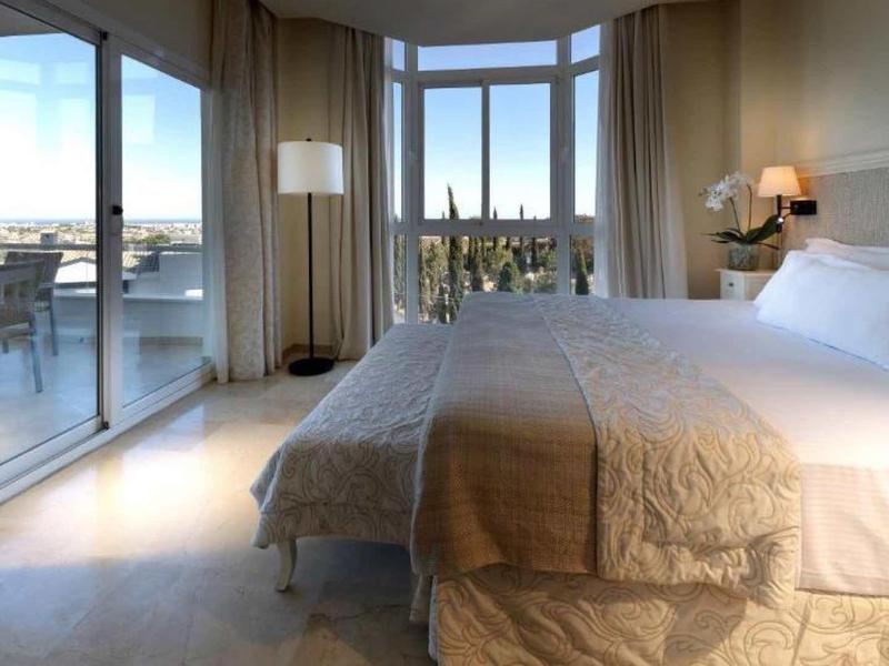 Bright hotel room with large bed and city view through floor-to-ceiling windows.