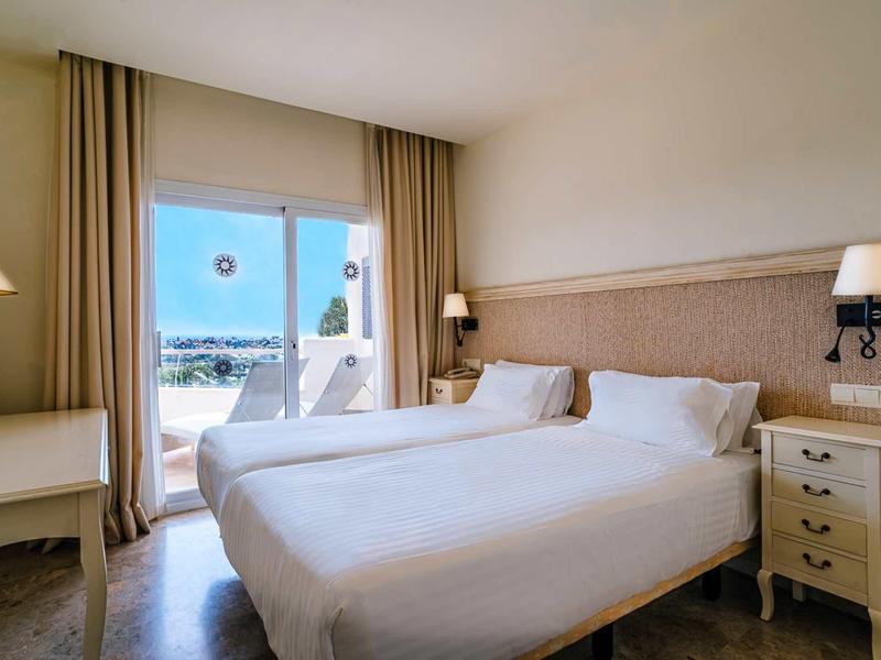 Cozy hotel room with double bed and view of terrace and sea.