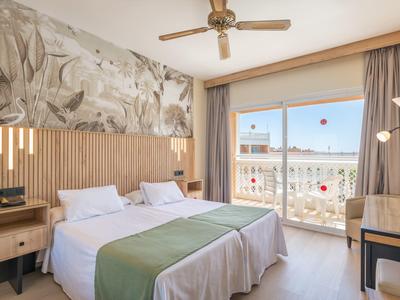 Bright hotel room with two single beds, balcony, and ceiling fan.