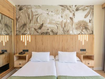 Modern hotel room with two single beds, wooden headboard, and floral wall decoration.