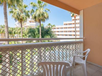 Balcony with two white plastic chairs overlooking palm trees and a hotel building.