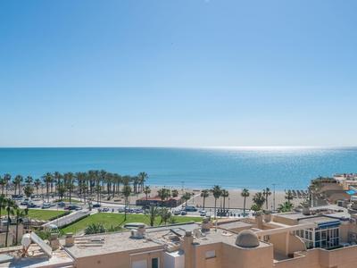 View of a hotel with sea, beach, and palm trees under clear blue sky