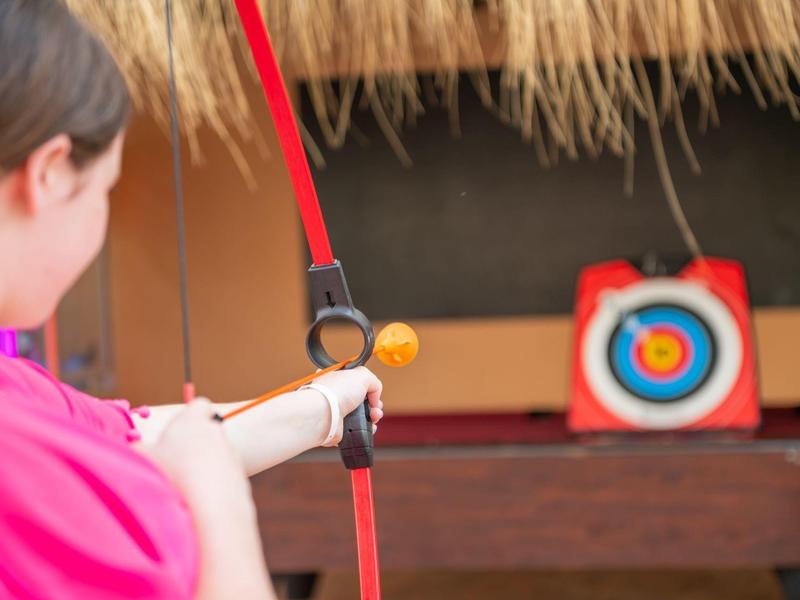 Person aiming a bow and arrow at a target in an indoor setting.