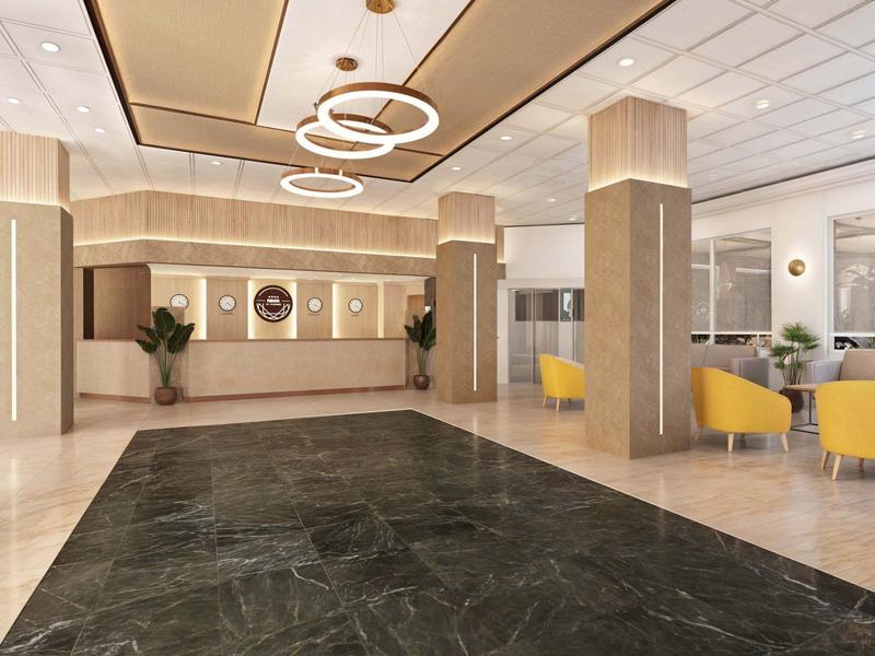 Modern hotel lobby with reception desk, plants, and yellow armchairs.