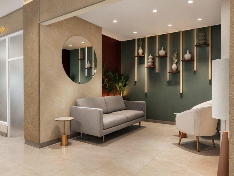 Modern hotel lounge with gray sofa, stools, and green accent wall with lighting.