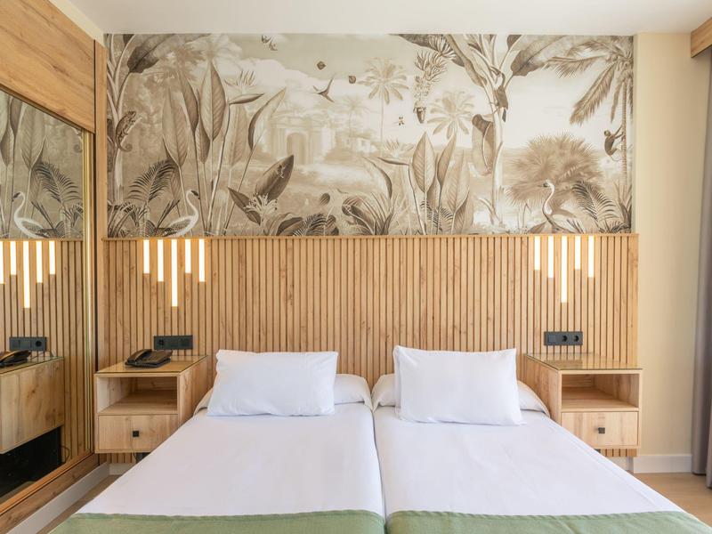 Modern hotel room with two single beds, wooden headboard, and floral wall decoration.