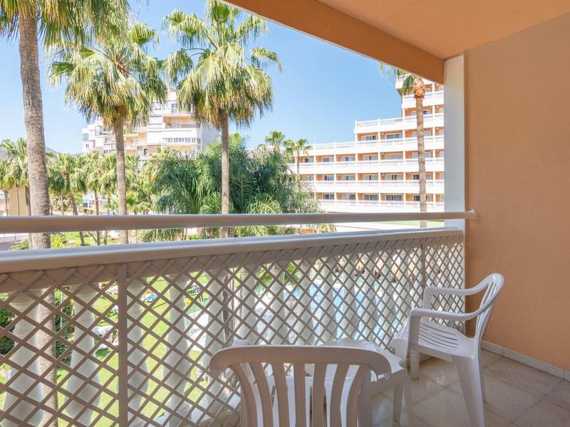Balcony with two white plastic chairs overlooking palm trees and a hotel building.