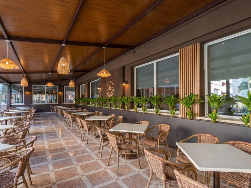 Covered terrace with tables, chairs, and green plants along the restaurant wall.