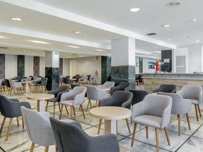 Modernes Café mit grauen Sesseln, runden Holztischen und heller, offener Raumgestaltung.