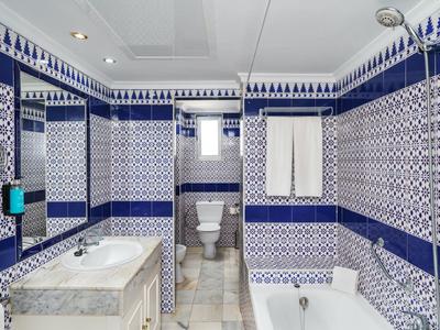 Bagno con piastrelle a motivo blu e bianco, vasca, lavabo, specchio e WC.
