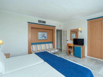 Camera d'hotel con due letti, passamaneria blu, mobili in legno e TV, luminosa e ordinata.