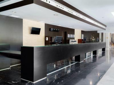 Reception moderna dell'hotel con lunga scrivania nera, computer e area salotto.