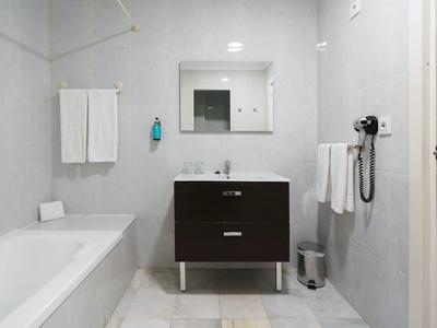 Bagno minimalista con vasca, mobile scuro, specchio, asciugamani e asciugacapelli.