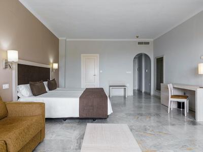 Ampia camera d'albergo con letto grande, divano, scrivania e decorazioni minimaliste in tonalità neutre.