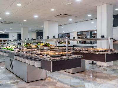 Ampio buffet dell'hotel con varie paste e frutta sotto luci a soffitto luminose.