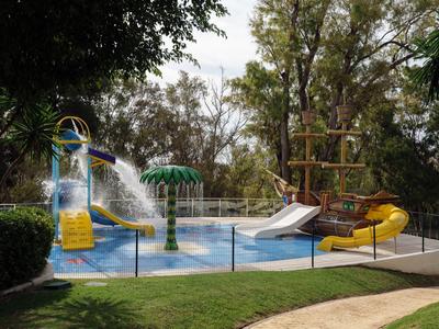 Leerer Wasserspielplatz mit Rutschen und Planschbecken in einem von Bäumen umgebenen Hotelgarten.