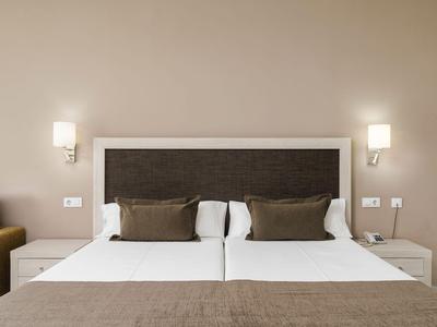 Modernes Hotelzimmer mit zwei Einzelbetten, weißen Laken und braunen Kissen neben Nachttischen und Wandlampen.