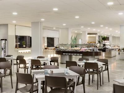 Heller und moderner Hotelrestaurantbereich mit zahlreichen Tischen und Stühlen.