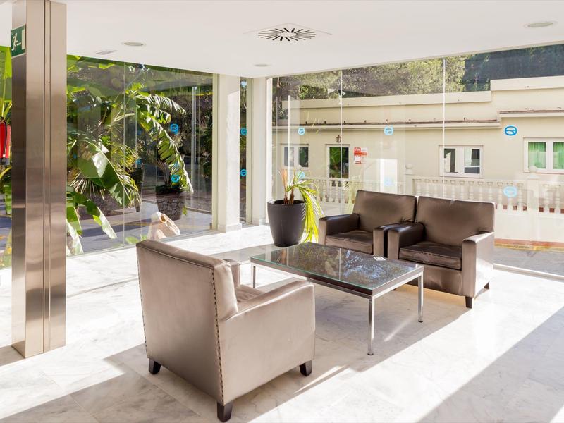 Hall moderno con divani marroni, pareti in vetro e tavolino con piante fuori.