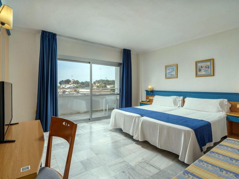 Camera d'hotel luminosa con letti singoli, tende blu, balcone e scrivania con TV.