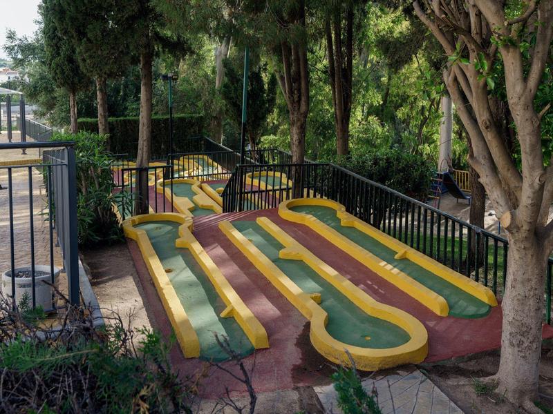 Percorso esterno di mini golf con due piste parallele verdi e gialle circondate da alberi e recinzione.