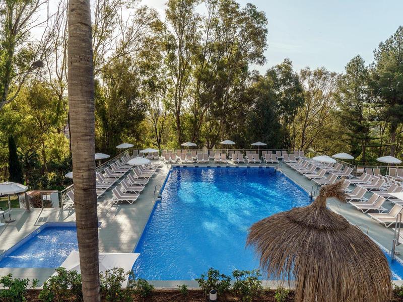 Piscina all'aperto con lettini e ombrelloni circondata da alberi in un resort.