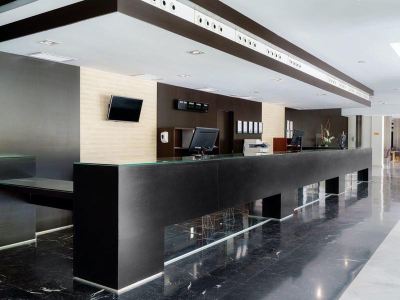 Reception moderna dell'hotel con lunga scrivania nera, computer e area salotto.