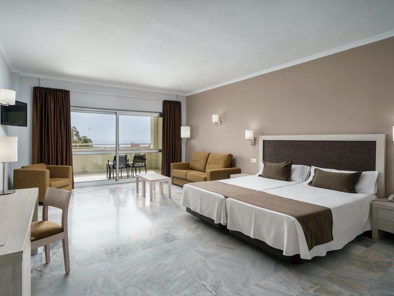 Camera d'hotel moderna con letto grande, zona salotto e balcone con vista esterna.