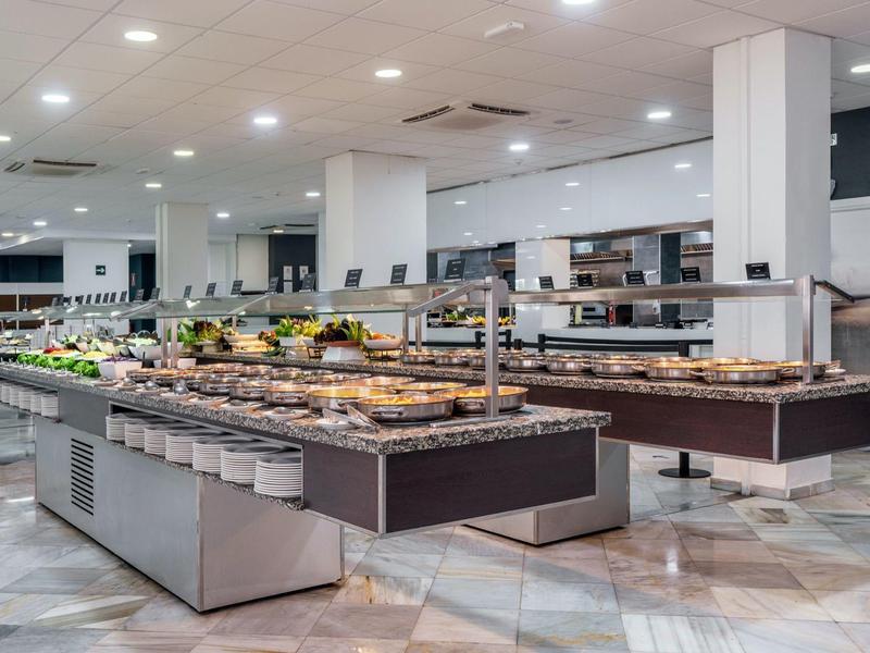 Ampio buffet dell'hotel con varie paste e frutta sotto luci a soffitto luminose.