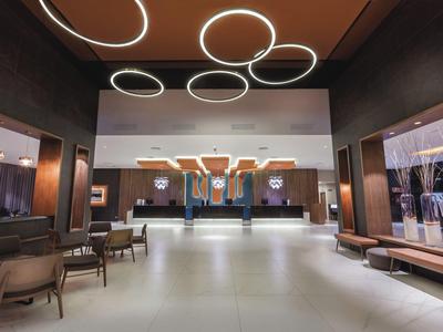Ampia hall di hotel con sedie, lampade rotonde e design moderno.
