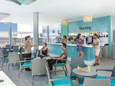 Bar colorato su una terrazza con clienti che godono del sole e delle bevande.