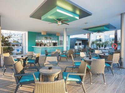 Terrazza dell'hotel con tavoli, sedie e bar, ambiente luminoso e accogliente.