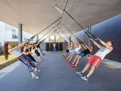 Gruppe von Menschen, die an hängenden Bändern in einem überdachten Außenbereich trainieren.