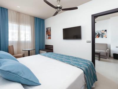 Camera d'hotel moderna con letto, TV a parete e poltrona vicino alla finestra.