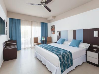 Camera d'hotel luminosa con letto matrimoniale, decorazioni blu e terrazza vetrata.