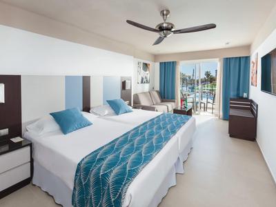 Camera d'hotel moderna con due letti, decorazioni blu e balcone con vista sul mare.