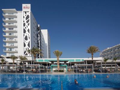 Moderner Hotelkomplex mit großem Pool und Sonnenschirmen unter klarem blauem Himmel.