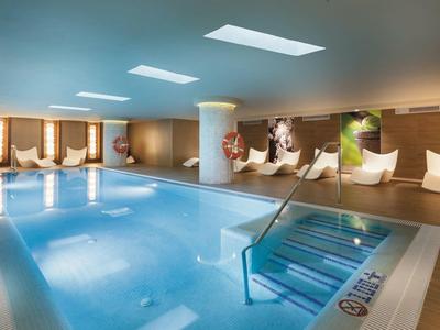 Piscina interna moderna con lettini bianchi e luce naturale.