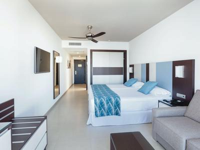 Modern eingerichtetes Hotelzimmer mit Bett, Sofa und minimalistischem Design in hellen Farben.
