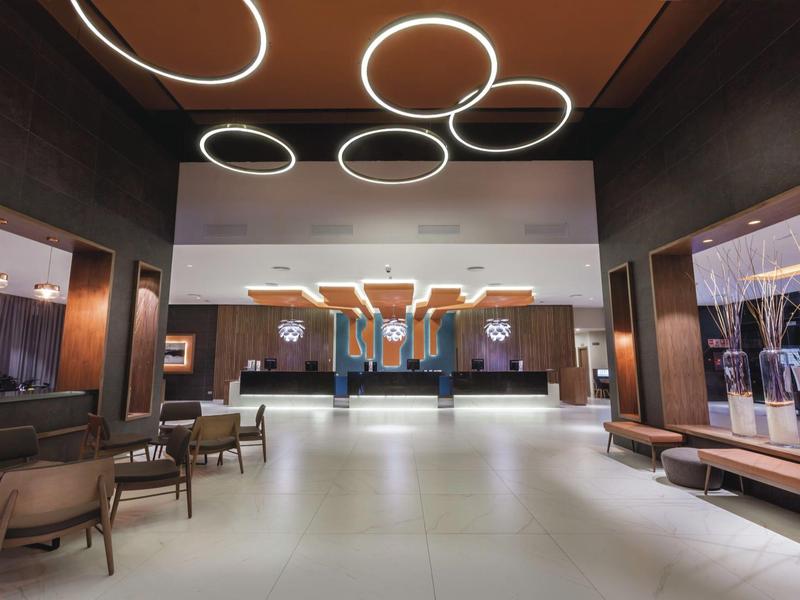 Ampia hall di hotel con sedie, lampade rotonde e design moderno.