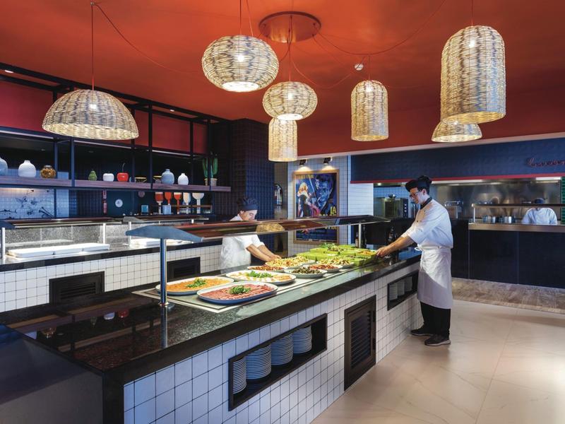 Buffet di un ristorante d'hotel con illuminazione calda e personale in uniforme bianca.