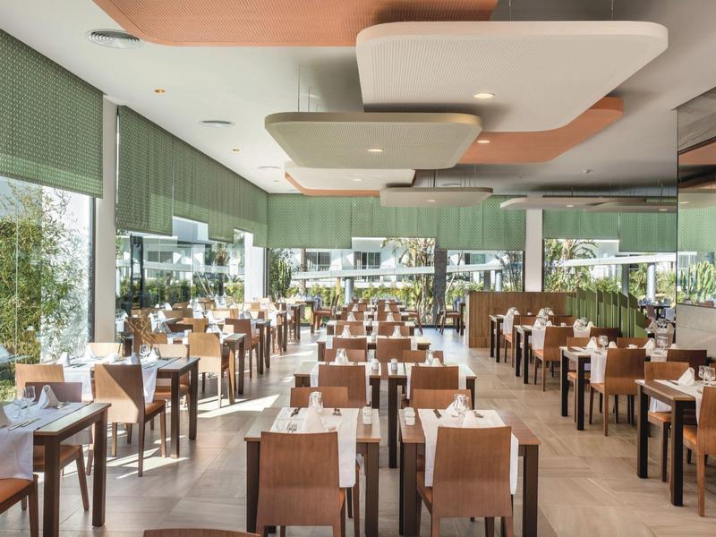 Sala da pranzo luminosa con tavoli in legno e grandi finestre con vista sul giardino.