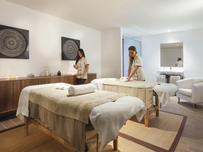 Sala massaggi elegante con due lettini e donna che prepara l'ambiente.