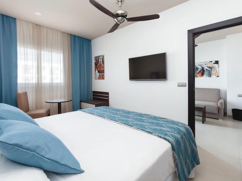 Camera d'hotel moderna con letto, TV a parete e poltrona vicino alla finestra.