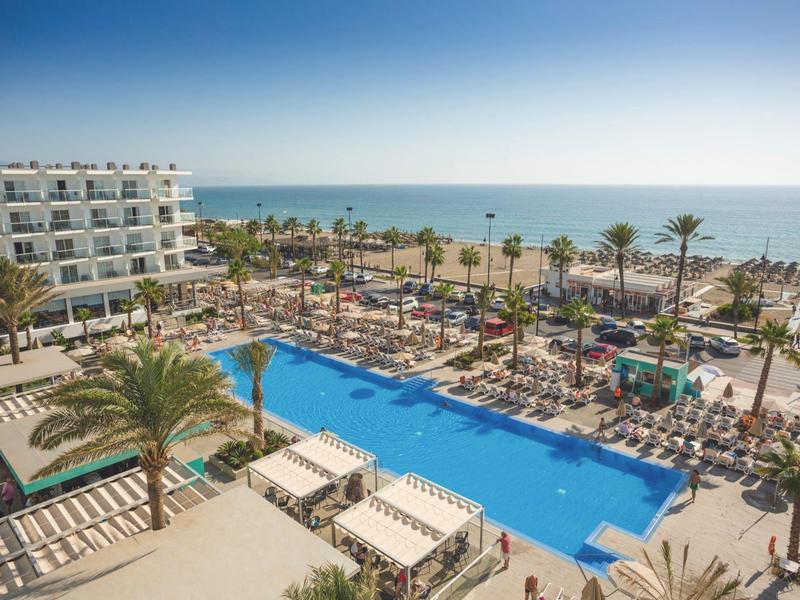 Piscina esterna con palme e vista mare vicino a un hotel.