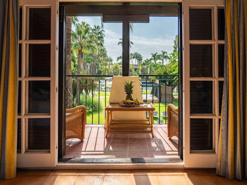 Vue d'une chambre sur un balcon avec une chaise longue et une végétation tropicale.