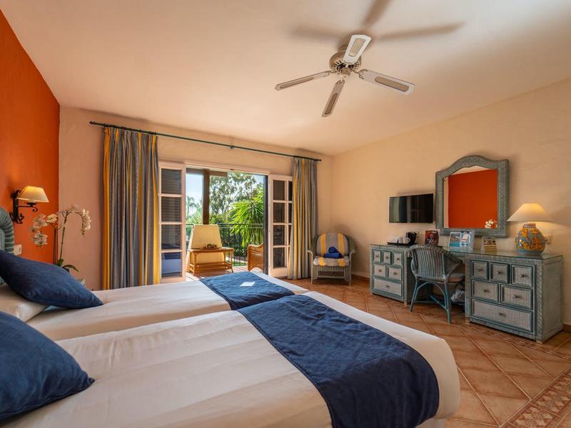 Chambre d'hôtel lumineuse avec deux lits, télévision satellite et balcon avec vue sur la verdure.