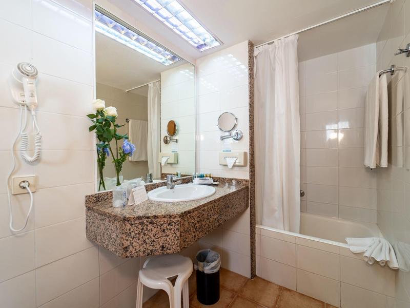 Salle de bain lumineuse avec lavabo en marbre, miroir, baignoire et serviettes.