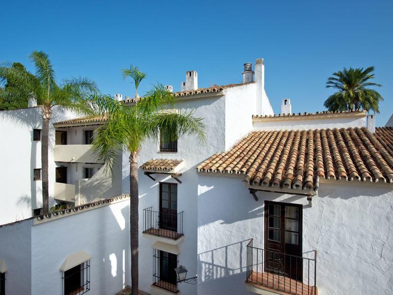 Bâtiments méditerranéens blancs avec toits en tuiles et palmiers sous un ciel bleu clair.