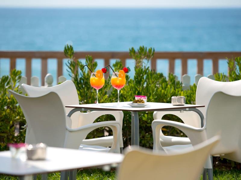 Terrasse avec chaises blanches, tables et deux cocktails orange avec vue sur la mer.